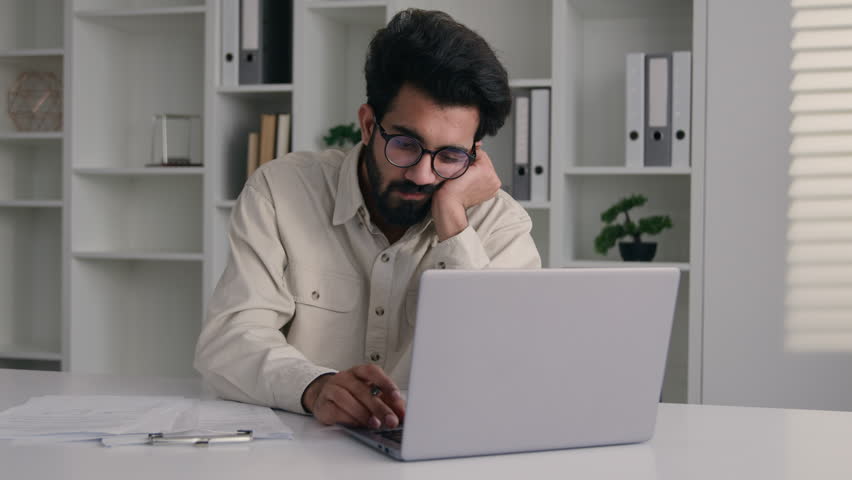 Tired Arabian muslim man overworked laptop remote job drowsy exhausted lazy Indian businessman ceo executive manager low energy monotone boring paperwork write business notes asleep overwork in office Royalty-Free Stock Footage #1106348279