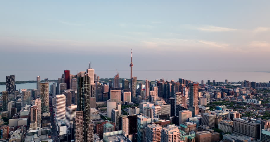 Aerial forward tracking  of Toronto cityscape, early evening, including CN Tower, lakeshore, and a mix of buildings, condos, and office towers. Cloudy evening sky adds to the atmospheric perspective. Royalty-Free Stock Footage #1106348947