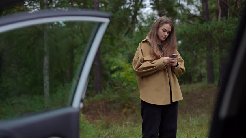 Anxious young woman standing in park at broken car with open door calling talking on phone. Portrait of worried Caucasian lady alone with damaged vehicle outdoors | Shutterstock HD Video #1106354443