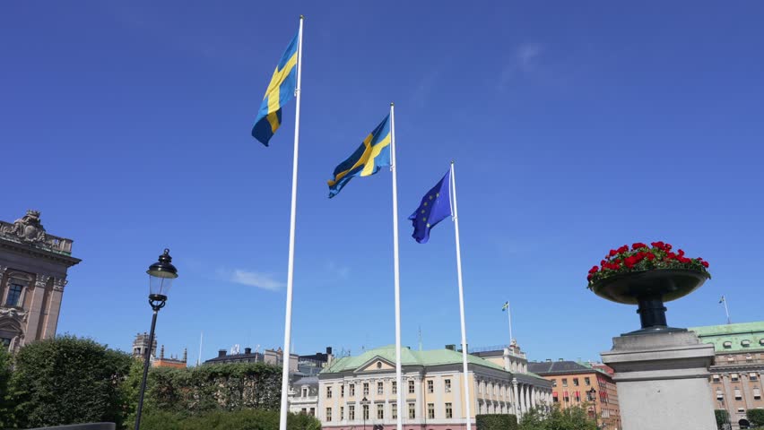 European Union and Sweden flag close together. Europe Union EU Friendship Flags on white pole in wind. Stockholm Swedish parliament Riksdagen on sunny day