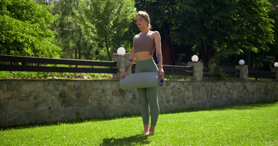 A blonde girl in a specially summer uniform spreads a special gray mat for playing sports on a green lawn in summer Royalty-Free Stock Footage #1106364039