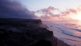 Aerial drone dolly shot of majestic Pacific Ocean Portuguese coastline. Cinematic purple and pink sunset, fluffy clouds over water. Inspiring nature aerial - Powered by Shutterstock - Get 15% off with code: PIKWIZARD15