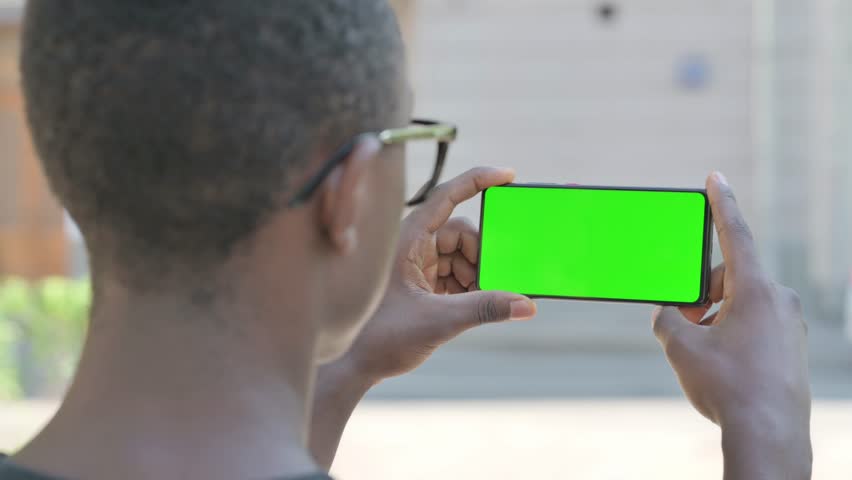 Young African Man Holding Phone with Green Screen Outdoor
