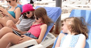 Teen girls on beach sun lounger play video games on tablet