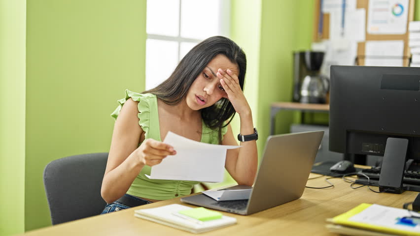 Young beautiful hispanic woman business worker using laptop reading letter looking upset at office