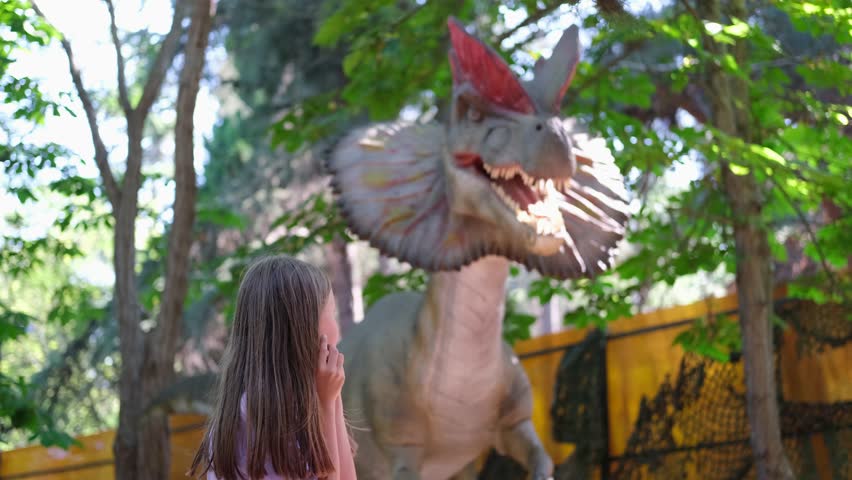 A child screams at the sight of a dinosaur. Teenage girl in dinopark.