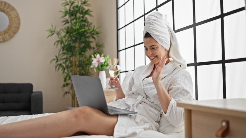 Young beautiful hispanic woman wearing bathrobe drinking champagne having video call at bedroom Royalty-Free Stock Footage #1106378575