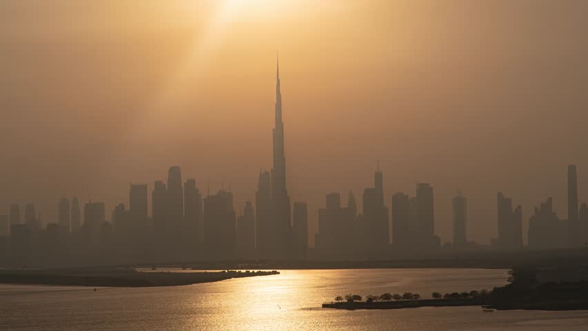 Sunset to night time lapse of Dubai skyline and Dubai Burj Khalifa silhouette while sun goes down with a beautiful golden sky while clouds are moving, Dubai, United Arab Emirates