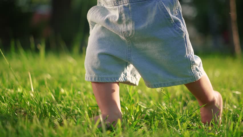 baby first steps. happy family kid dream concept. baby walks on the grass learns to walk in the city park close-up. baby first steps in nature. dad teaches son to walk lifestyle