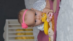Vertical video. Happy baby girl playing with toy while resting on tummy at home, slow motion