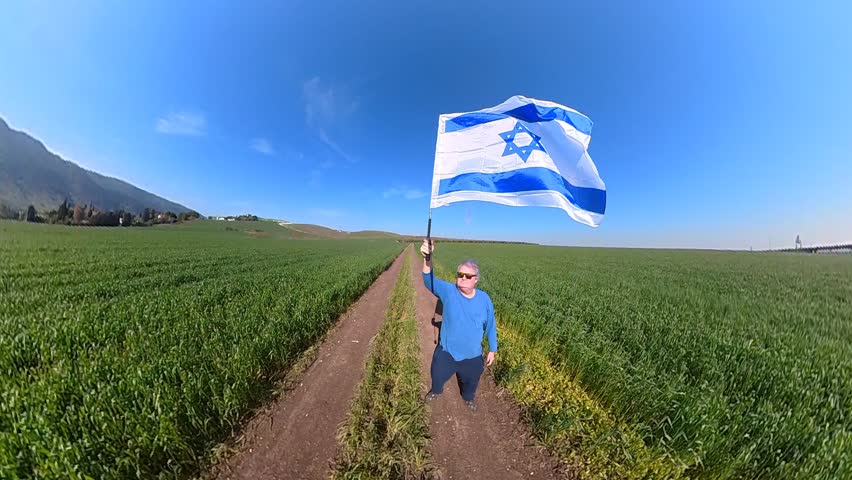 A man waving the flag of Israel in circles in a green field for independence patriotism and success Royalty-Free Stock Footage #1106384389