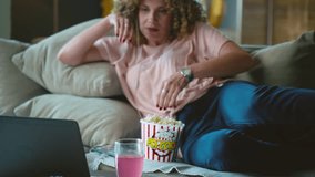 Satisfied happy woman lying on her comfortable couch and enjoying the weekend, eating popcorn and watching movie or series on laptop - Powered by Shutterstock - Get 15% off with code: PIKWIZARD15