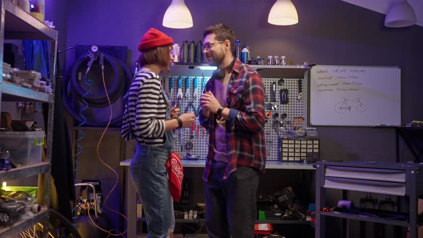Man and woman funny dancing at garage. Mechanics cheerfully singing at workshop. Male and female using wrenches like microphones. Man and woman having relax at work shop.