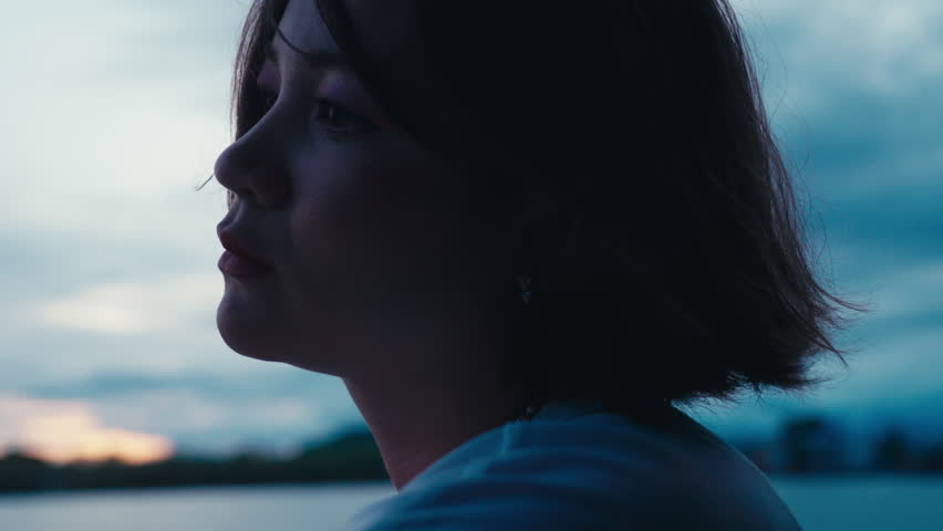 beautiful sad girl looking at dark evening sky on a lake shore. Close-up portrait of pensive thoughtful woman suffering outdoors. Lonely female person feeling blue and gloomy. Depression and stress. Royalty-Free Stock Footage #1106388925