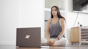 young Latin woman in a virtual reunion with her computer in sportswear on a yoga mat talking
