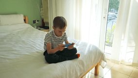 6 years boy playing video game on smartphone sitting on a bed in the morning. 4k slow motion video footage