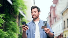 Happy male tourist uses a credit card and mobile phone make purchases, pay for services or book a hotel or accommodation. order using smartphone app while standing on the city street Outdoors Outsite - Powered by Shutterstock - Get 15% off with code: PIKWIZARD15