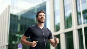 Handsome bearded male runner running on a modern urban background of buildings a city street. Sporty man jogger in headphones jogging outdoors look at result a fitness tracker bracelet or smartwatch - Powered by Shutterstock - Get 15% off with code: PIKWIZARD15