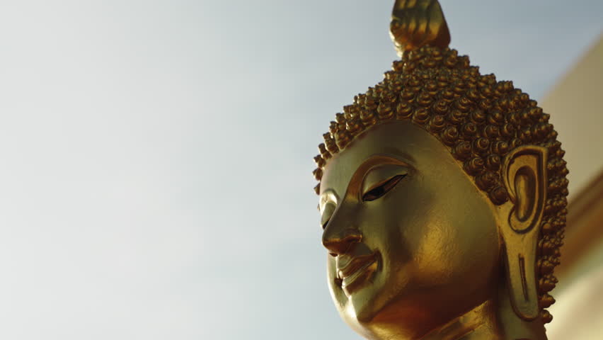 Zoom out camera moves with parallax effect from the face of golden sitting Buddha statue on the mountain of the temple complex with a Buddhist stupa. Sunrise wide angle shot Royalty-Free Stock Footage #1106405105