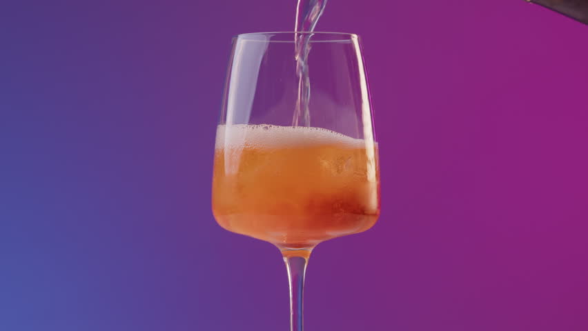 Hand of a professional bartender pours prosecco from bottle into long drink glass with aperol. Preparation of a summer cocktail aperol on the bar with neon lighting and blue purple background Royalty-Free Stock Footage #1106405129