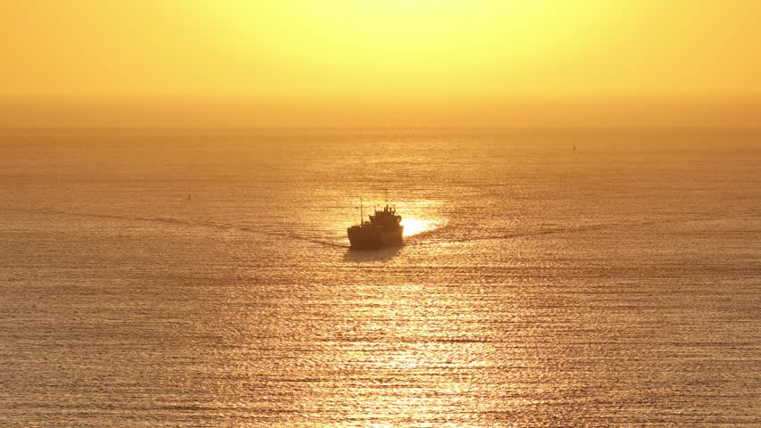 Zoomed drone panning shot of a cargo vessel sailing over the North Sea during sunset