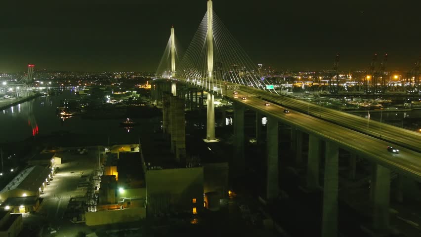 Aerial flyby of lit bridge in Long Beach California | Ship sailing underneath | Night time