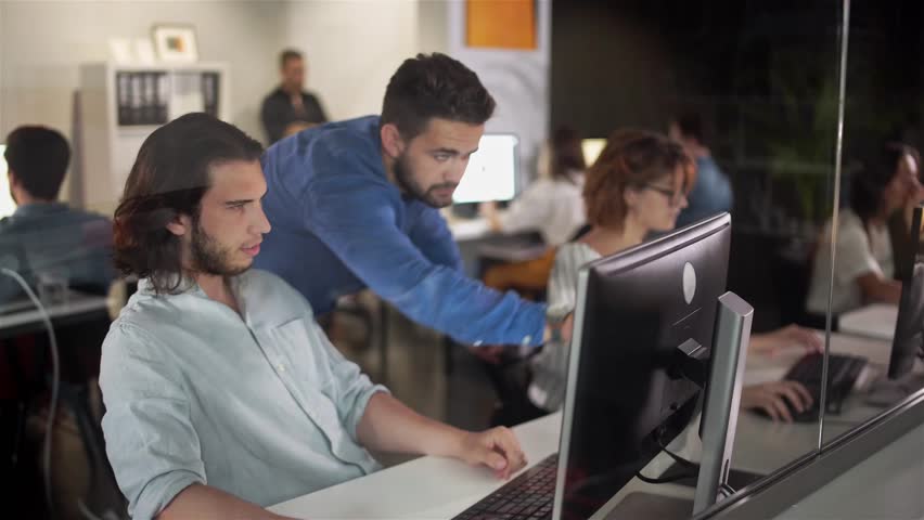 Coworkers looking at a computer and talking about work. Team of colleagues brainstorming together while working on the computer. Men colleagues discuss online project look at pc screen