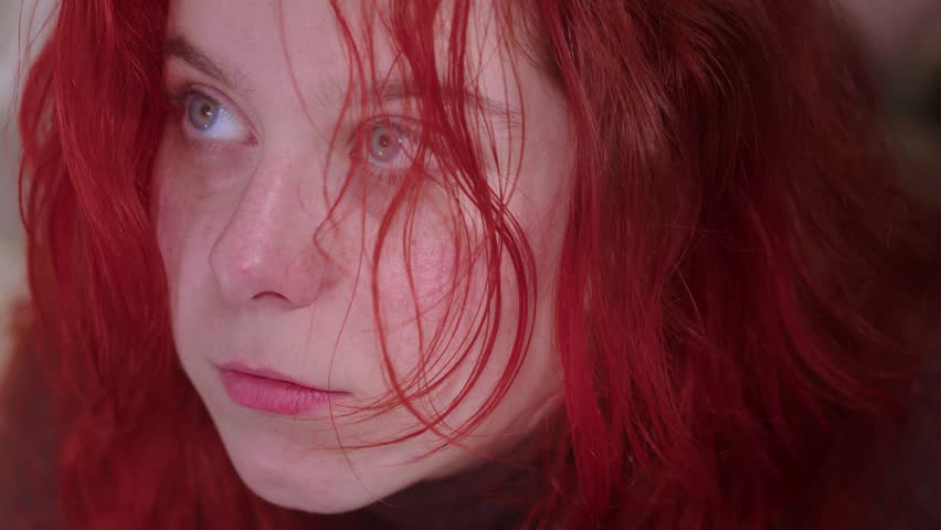 Thoughtful girl moves her red hair with a puff of breath. She has a fair complexion and big eyes. Close up and slow mo shot  Royalty-Free Stock Footage #1106413529