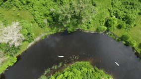 Canoeing along a steep bend in a small river among the grass. Smooth video shooting from a drone in cloudy weather.