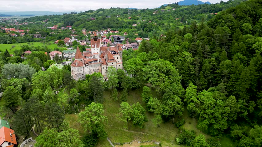 Medieval Bran Castle - Romania, aerial drone perspective. Drone descending . In background is the village of Bran. Known as Dracula's Castle, it is visited annually by many foreign tourists.  Royalty-Free Stock Footage #1106416483