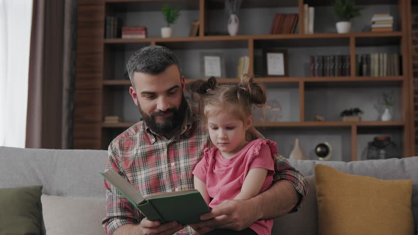Young father and daughter read intersting book at home. Loving parent bearded man teaches his preschool child to read. Daddy reading fairy tale story. Parenthood, love and happy family concept. Royalty-Free Stock Footage #1106416499
