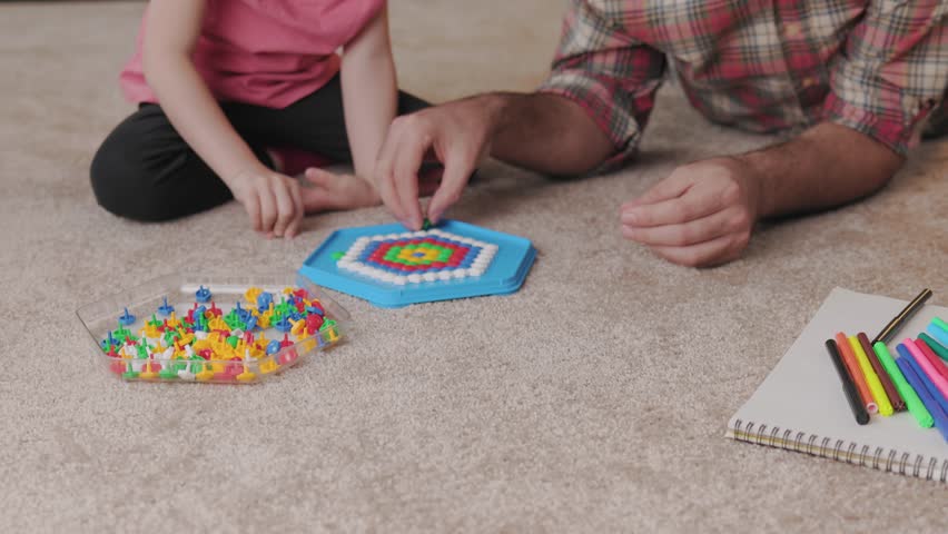 Young handsome father and cute daughter playing together. Dad and child making a puzzle with mosaic pegboard lying on the carpet at home. Educational toys for children. Home leisure. Father's day. Royalty-Free Stock Footage #1106416501