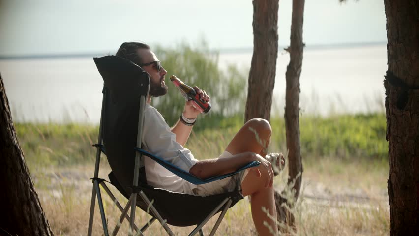 Man Drinking Chilled Beverage. Calm Beer Enthusiast Leisure Time. Relaxing Tourist Drinking Beer At Serene Atmosphere. Outdoor Relaxation With Bottle Beer. Weekend Chill With Cold Beverage Enjoyment Royalty-Free Stock Footage #1106417453