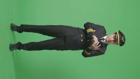 Full Body Of Asian Man Pilot Waving Hand Having A Video Call On Smartphone While Standing In The Green Screen Background Studio
