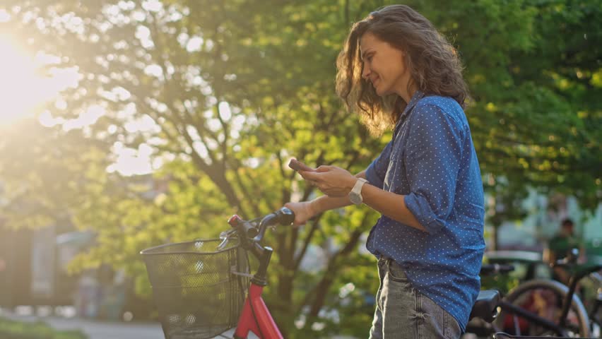 A young Caucasian woman using a phone while standing next to her bicycle in the city street.