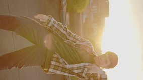 Vertical video. Caucasian male handsome dancer performing hip hop outside on the roof at sunset. Brunette man enjoying dance,looking at camera. Guy showing amazing gestures and movements