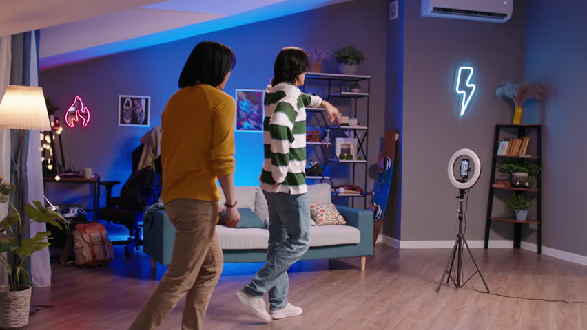 Long-haired guys recording dance reels. Stylish fashionable trendy hipsters Asian teen guys dance in front of camera for videos on social networks record cool reels, stories. Side view of dancing guys