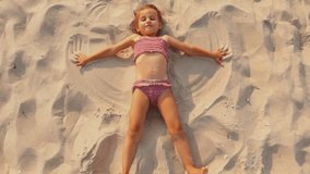 A child playing in a brown swimsuit lying on the beach on the sand makes an snow angel - Powered by Shutterstock - Get 15% off with code: PIKWIZARD15