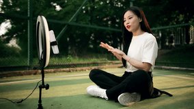 Blogger recording video at sports field Using smartphone outdoor. Beautiful asian woman blogger broadcasts live on a social network. The girl is blogging, reviewing products