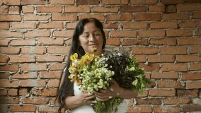 Horizontal open portrait of a Latina woman with a bunch of medicinal herbs and flowers. Defocused bricks background. Taken in Merida, Venezuela. Concept of peoples and traditions. real people video 4K