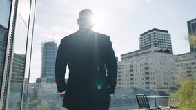 Rear back view following handsome male businessman in suit walks roof top terrace in office building overlooking modern city downtown cityscape with high-rise skyscrapers backlit with bright sunlight - Powered by Shutterstock - Get 15% off with code: PIKWIZARD15