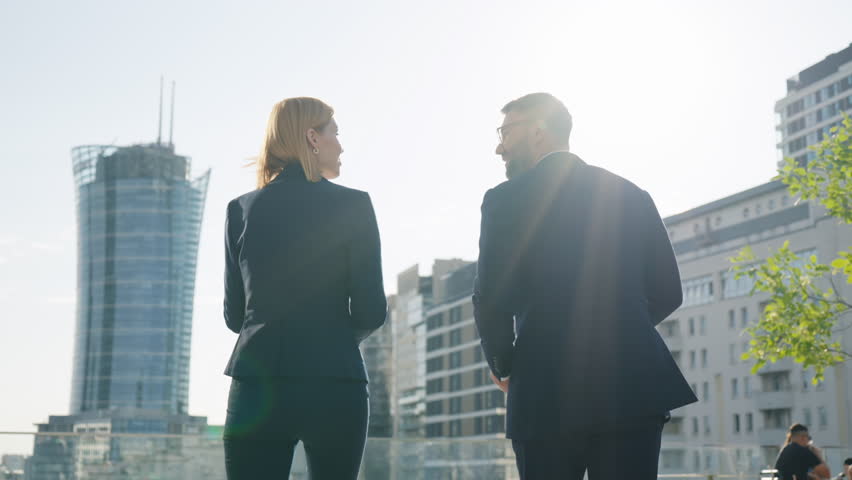 Back view two successful business partners happy male female handshaking deal gesture celebrate success walk along office building rooftop overlooking high-rise skyscrapers, sunny day, bright sunbeams Royalty-Free Stock Footage #1106431611