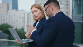 Handheld portrait shot two business partners bearded man blonde woman standing outdoors office building terrace or balcony discuss upcoming project deals using laptop. Corporate people city downtown - Powered by Shutterstock - Get 15% off with code: PIKWIZARD15