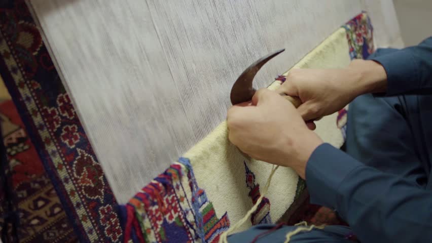 A man weaves a traditional Arabic carpet of multicolored wool. Weaving and making handmade carpets close-up. Male hands with a traditional Arabic knife cut the thread while weaving a carpet Royalty-Free Stock Footage #1106442605