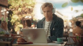 Young Stylish Freelance Designer Having an Online Conversation with a Client. Content Creator in Headphones Using Laptop Computer to Work Remotely from a Quiet City Restaurant Summer Terrace - Powered by Shutterstock - Get 15% off with code: PIKWIZARD15
