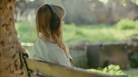 Lonely lady on park bench under tree with headphones listening to music - Powered by Shutterstock - Get 15% off with code: PIKWIZARD15
