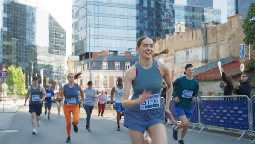 Slow Motion of a Diverse Group of People Running a Marathon in a City During the Day. Active and Fit Smiling Female Runner Competing to Reach the Finish Line, Supported by Friends and Family Royalty-Free Stock Footage #1106455829