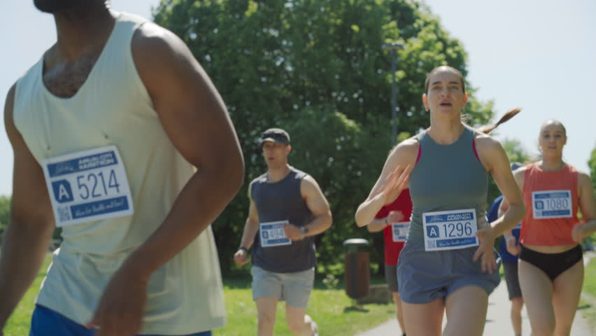 Slow Motion Portrait of a Woman Running and Participating in a Marathon in a Park. Strong Athletic Female Jogger Racing Other Runners with Determination for the First Place in the Finish Line