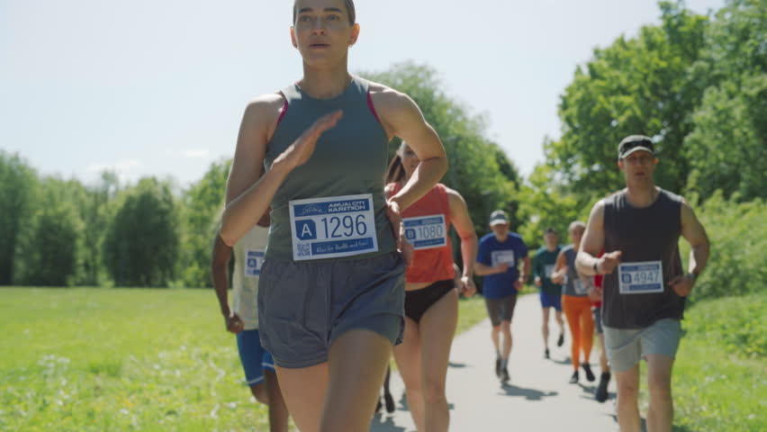 Slow Motion Portrait of a Woman Running and Participating in a Marathon in a Park. Strong Athletic Female Jogger Racing Other Runners with Determination for the First Place in the Finish Line