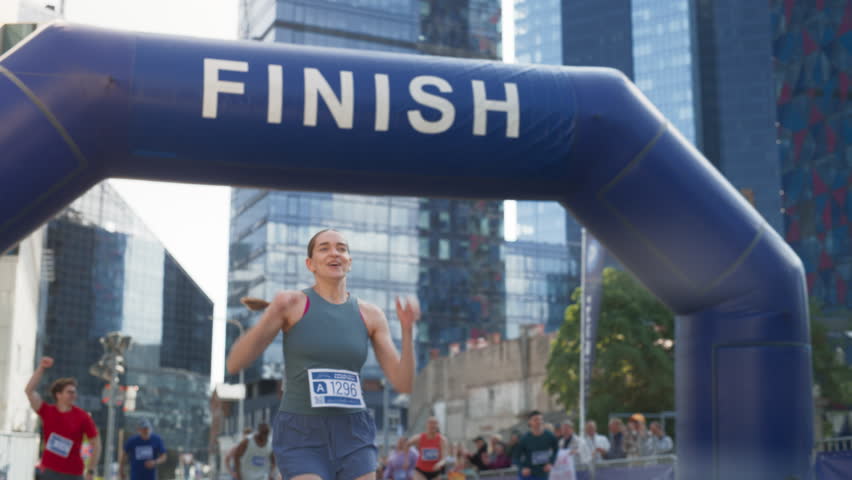 Slow Motion Portrait of a Happy Female City Marathon Runner Crossing the Finish Line and Celebrating her Victory. Female Race Winner Achieving her Goal and Enjoys her Accomplishement Royalty-Free Stock Footage #1106455929
